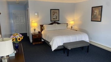 Habitación de hotel ordenada con una cama grande, lámparas de noche, una mesita con un florero y un banco.