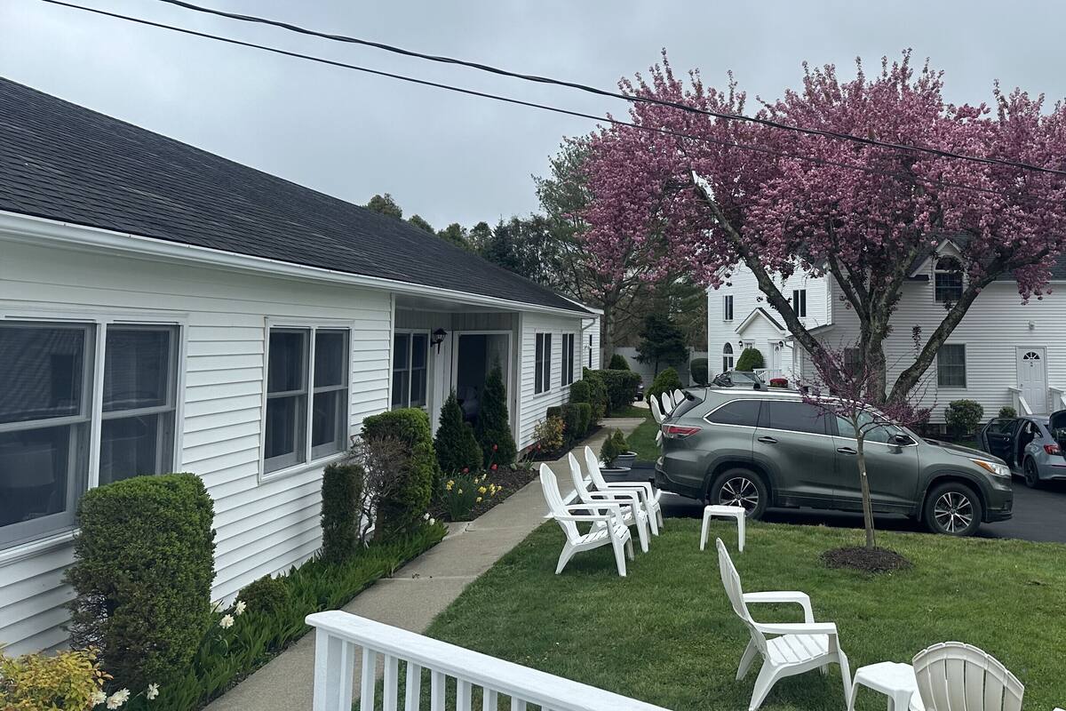 A residential house with a porch, a lawn, and a car parked in the driveway.