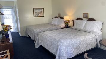 A hotel room with two beds, a desk, a chair, a lamp, and a vase with flowers.