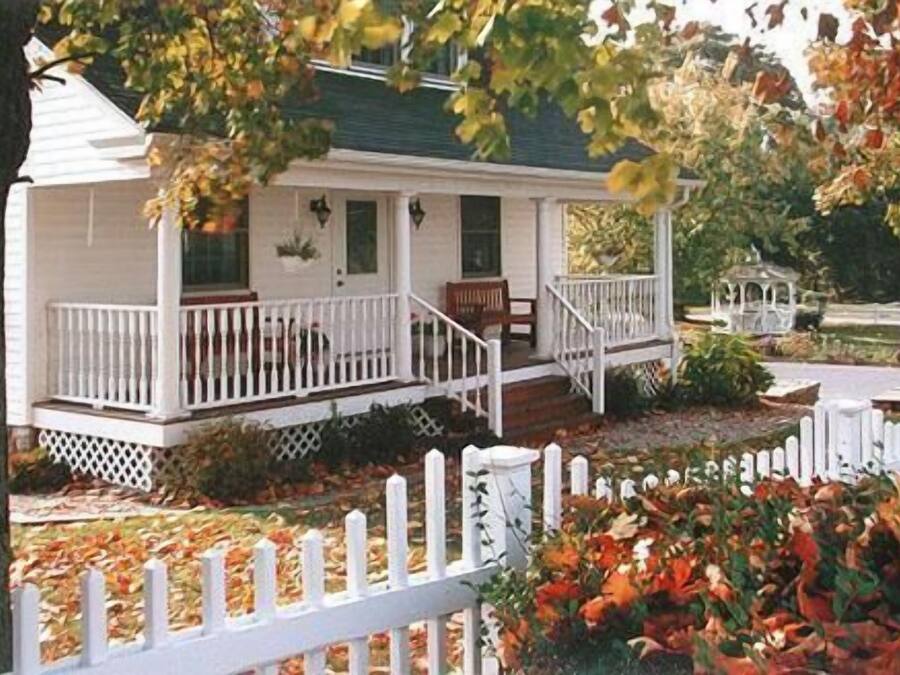 Een twee verdiepingen tellend huis met een veranda, een voordeur en een kleine tuin met een witte hek.'