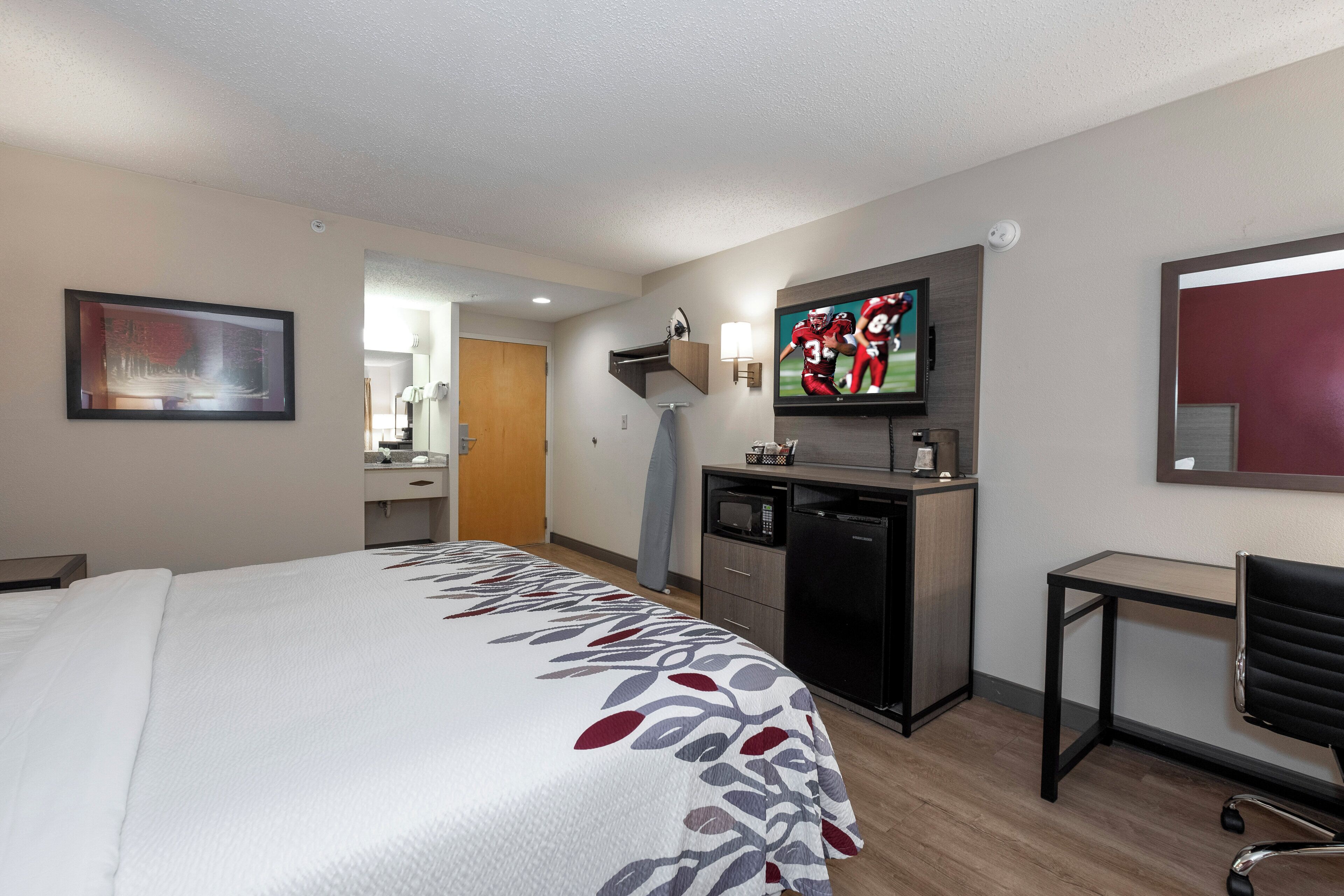 A hotel room with a large bed, a desk, a microwave, a television, and a small table.
