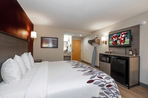 Una habitación de hotel con una cama grande, un televisor de pantalla plana montado en la pared, un escritorio con microondas y una pequeña cocina americana.
