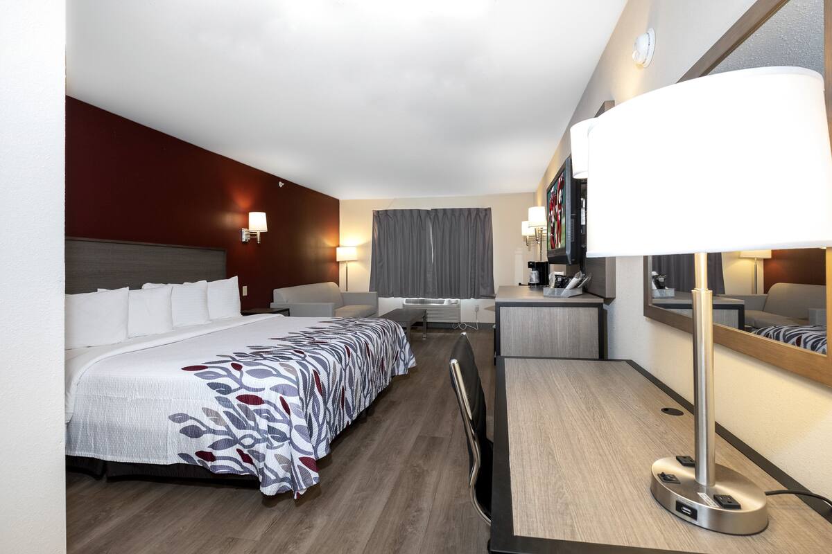 Ein Hotelzimmer mit einem großen Bett, einem Schreibtisch, einem Stuhl, einer Schreibtischlampe und einem Spiegel.