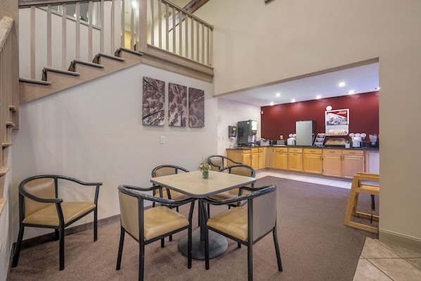 A dining area with a table and chairs, a kitchen in the background, and a staircase. - Red Roof Inn Clifton Park (Clifton Park)