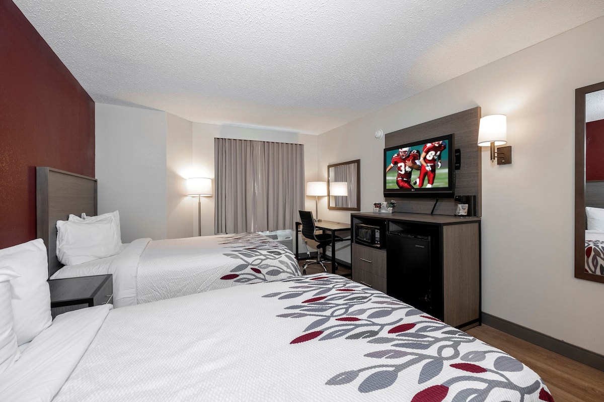 Ein Hotelzimmer mit zwei Betten, einem Schreibtisch, einem Fernseher und einer Mikrowelle.