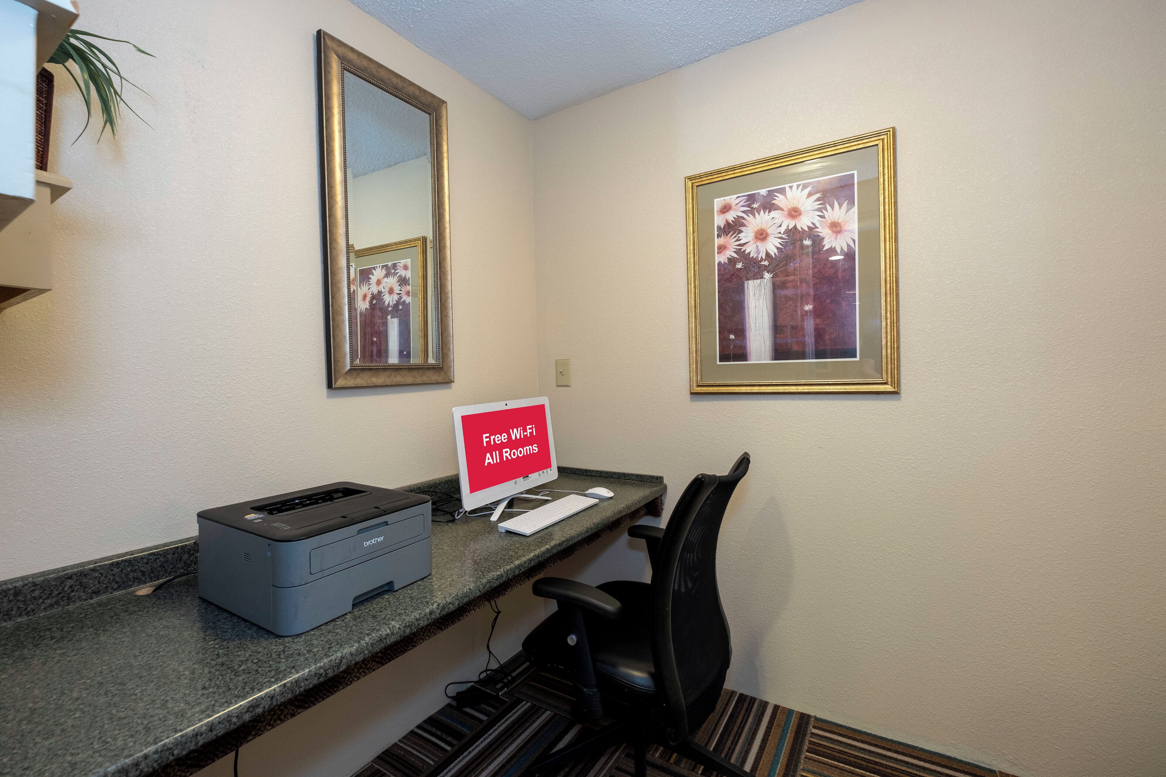 A hotel reception area with a desktop computer, a printer, and a sign indicating free Wi-Fi availability.