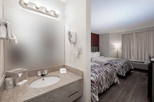 Habitación de hotel con lavamanos de granito, un espejo, teléfono, cama con colcha estampada y ventana con cortinas.
