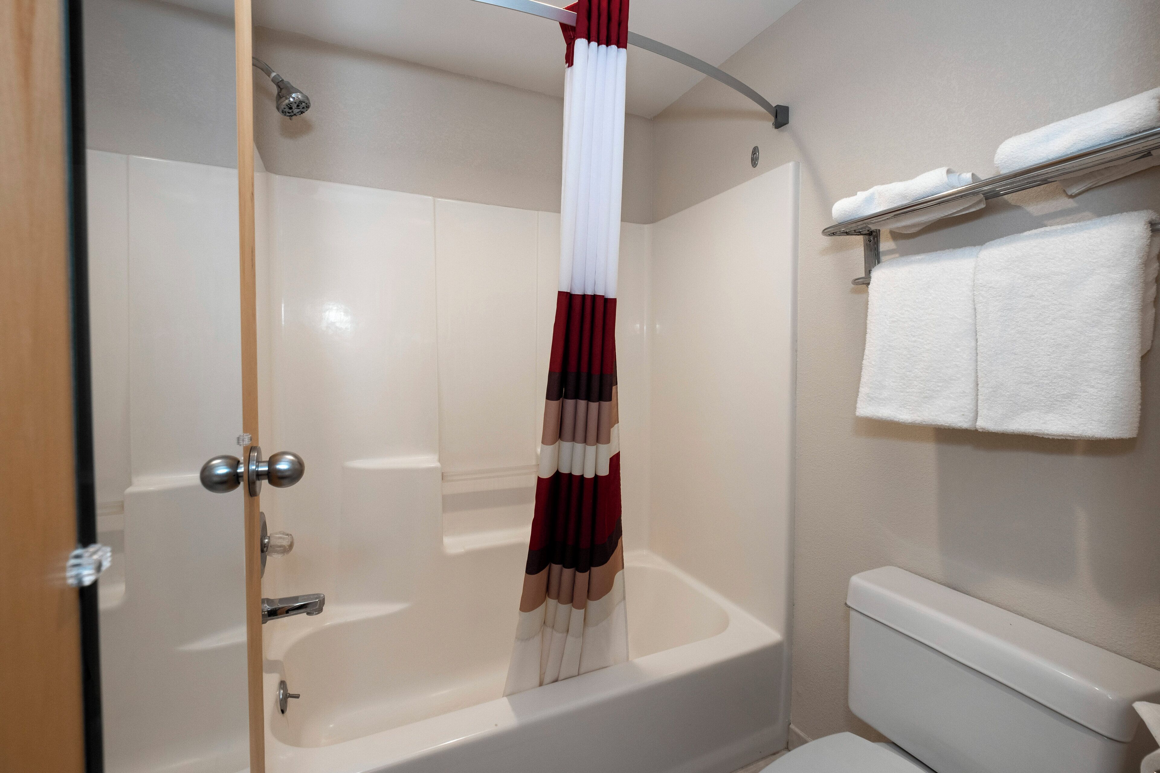 Et badeværelse med badekar, bruseforhæng, et håndklædetørrestativ med håndklæder og toilet.