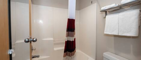 Un baño con bañera, cortina de ducha, toallero con toallas y un inodoro.