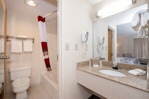 Et moderne badeværelse med toilet, bruser og vask. Der er håndklæder på en hylde og et spejl over vasken.