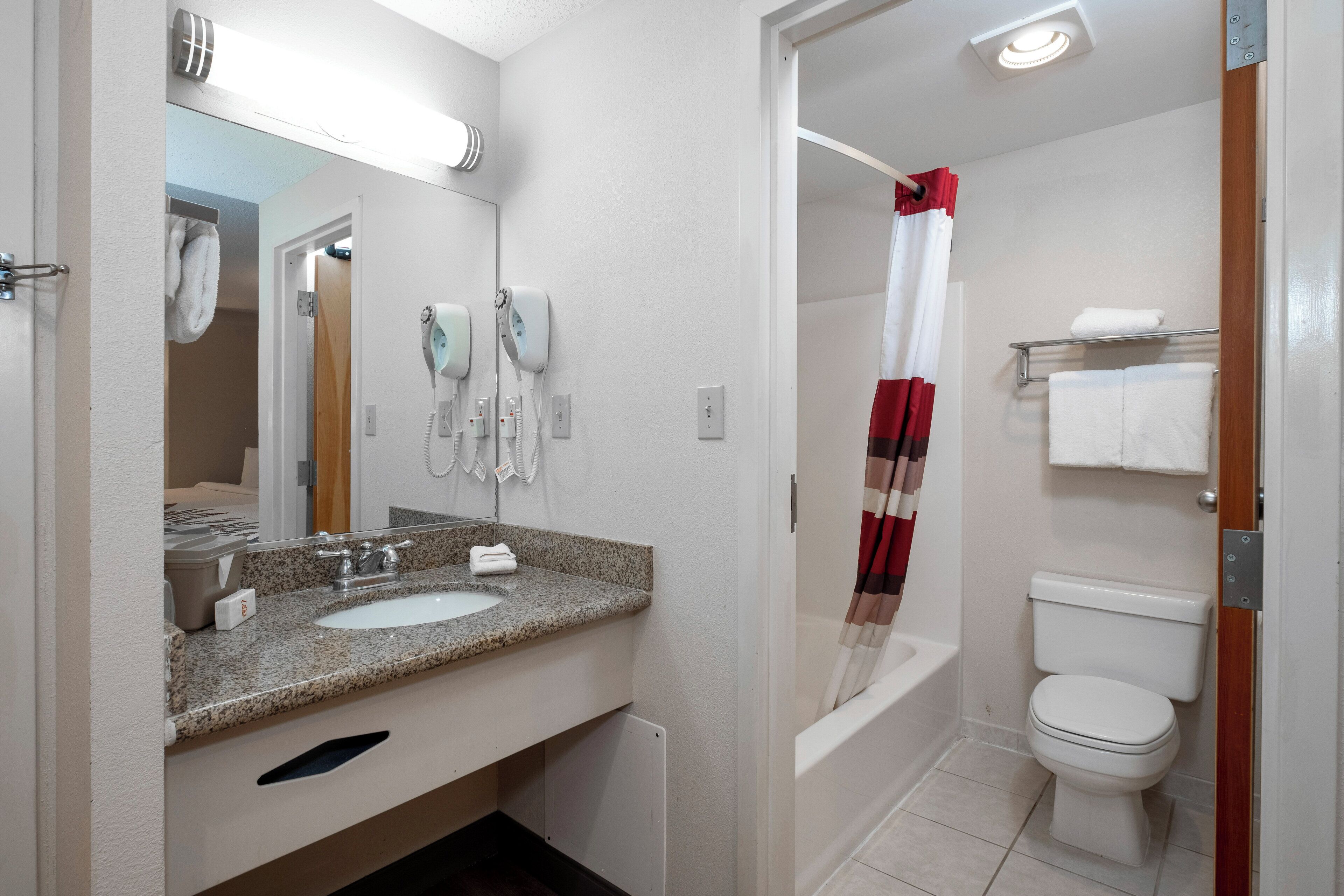 A bathroom with a sink, mirror, hairdryer, and toilet.