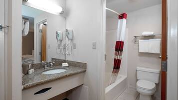 A bathroom with a sink, mirror, hairdryer, and toilet.