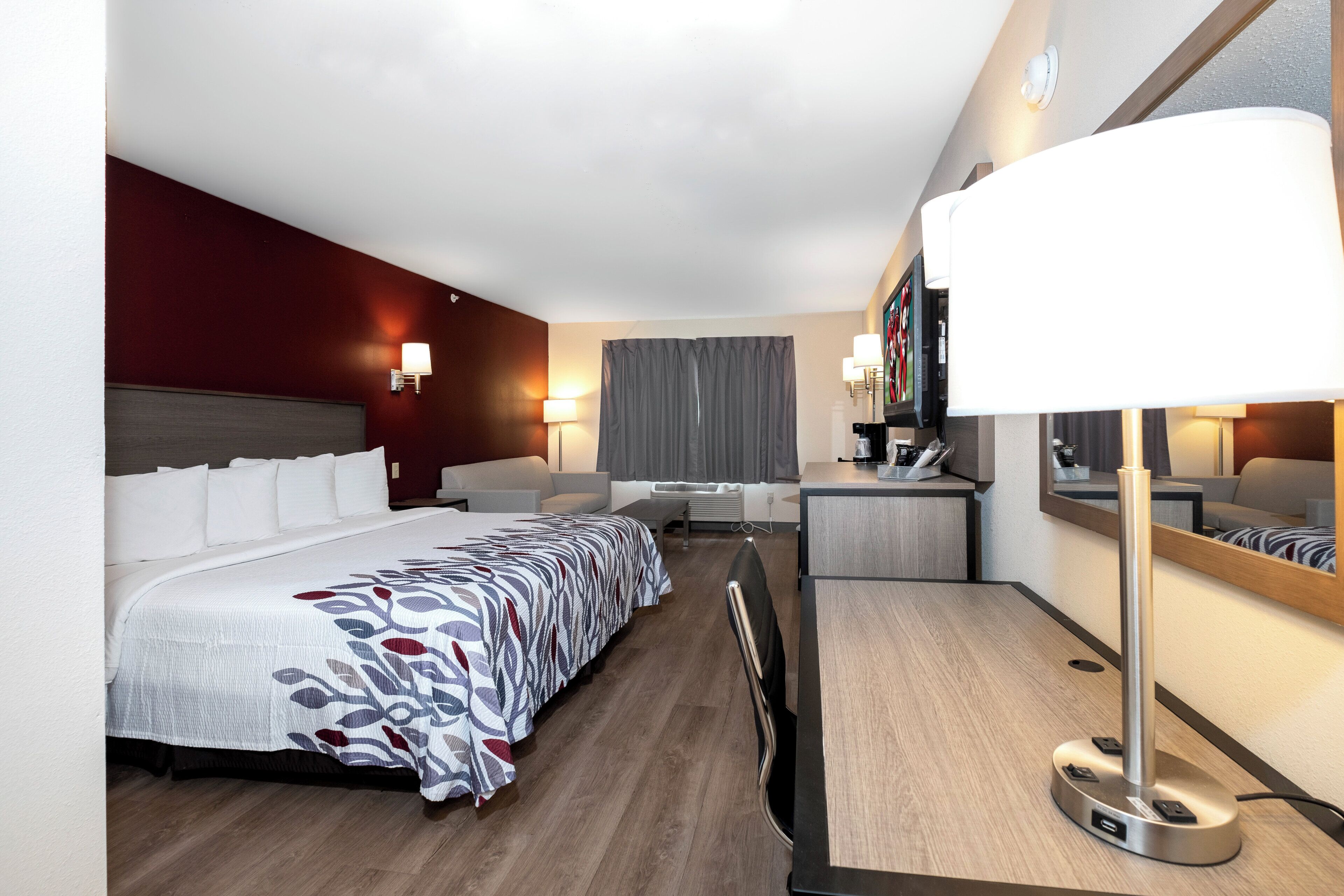 Een hotelkamer met een bed, een bureau, een stoel, een televisie en een spiegel.