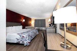 Una habitación de hotel con cama, escritorio, silla, televisor y espejo.