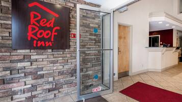 A Red Roof Inn entrance with a glass door, stone wall, and a red carpet leading inside.