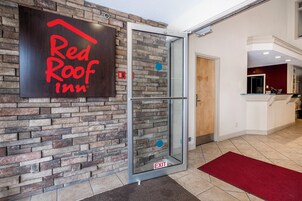 Entrada de Red Roof Inn con puerta de cristal, pared de piedra y una alfombra roja que lleva al interior.