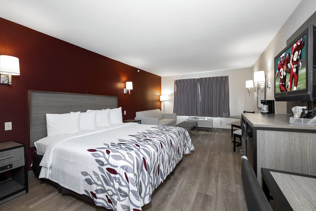 Ein Hotelzimmer mit einem großen Bett, einem Schreibtisch, einem Sessel und einem Fernseher.