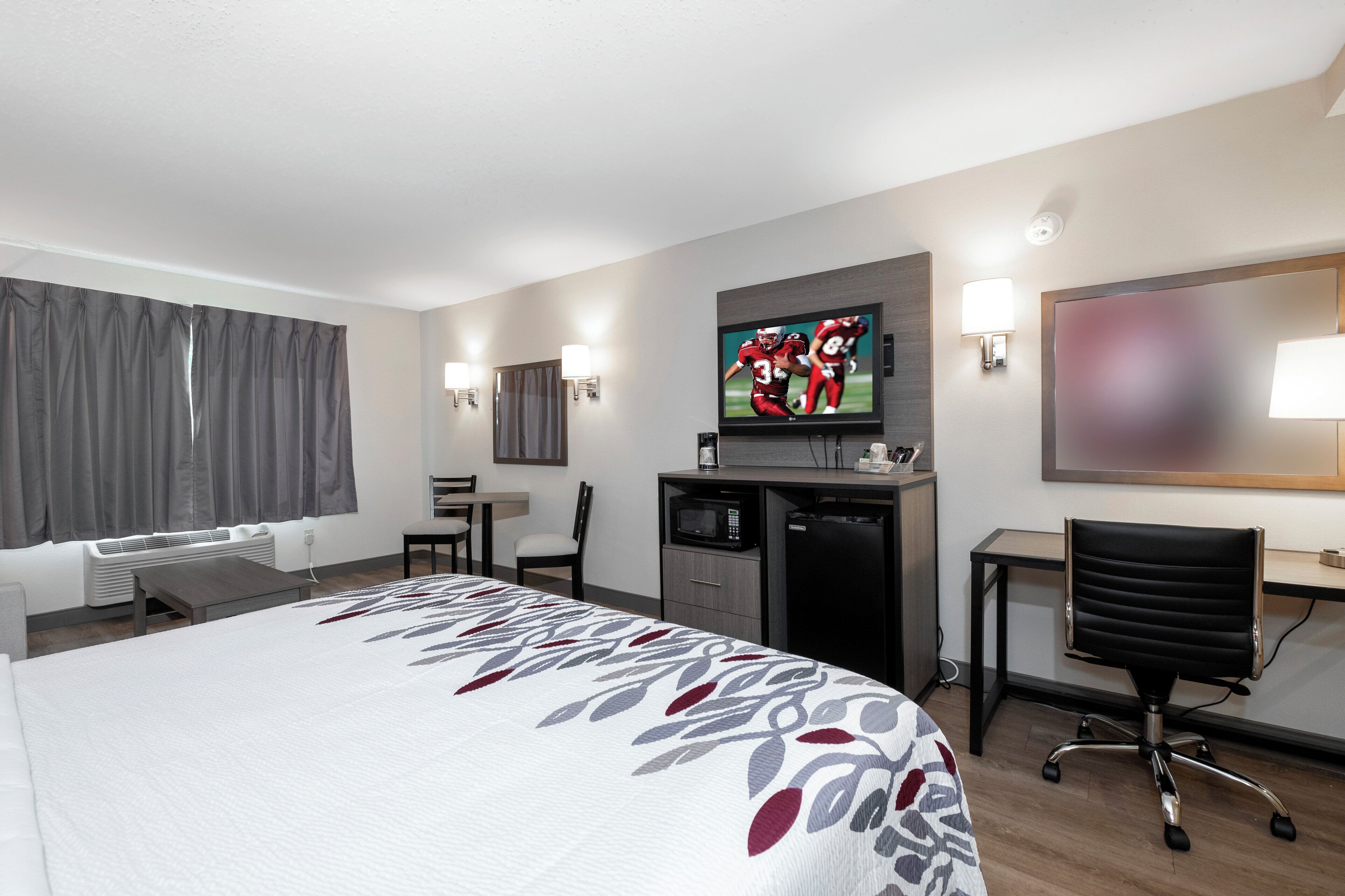 A hotel room with a bed, a desk, a TV, a chair, and a microwave.