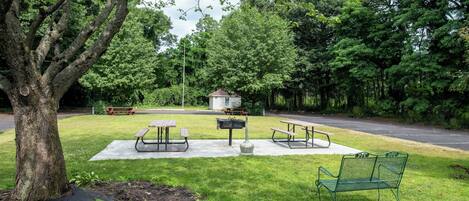 Un parque con mesas de picnic, un banco y un pequeño cobertizo.