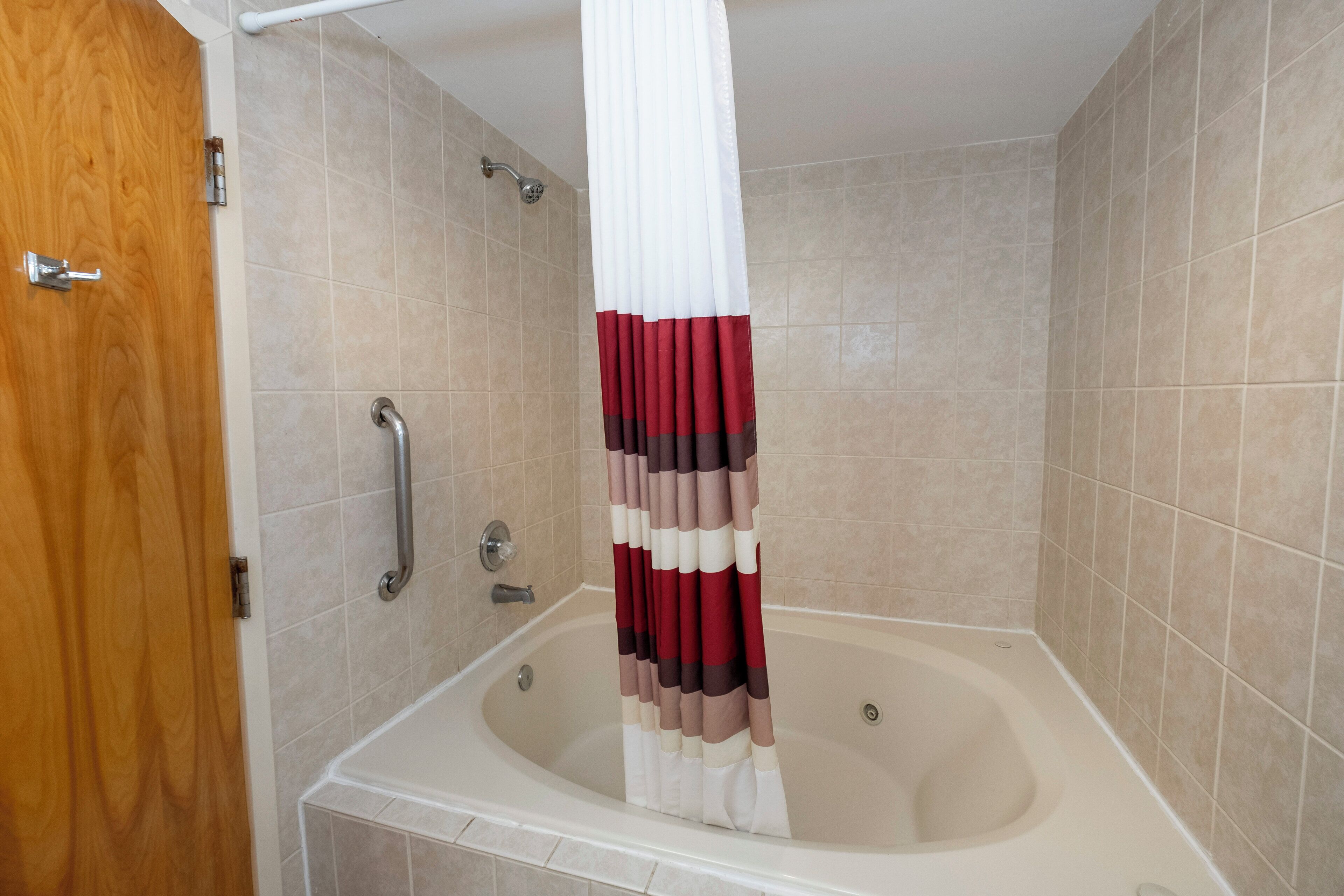 A bathroom with a bathtub, a shower curtain, and a handrail.