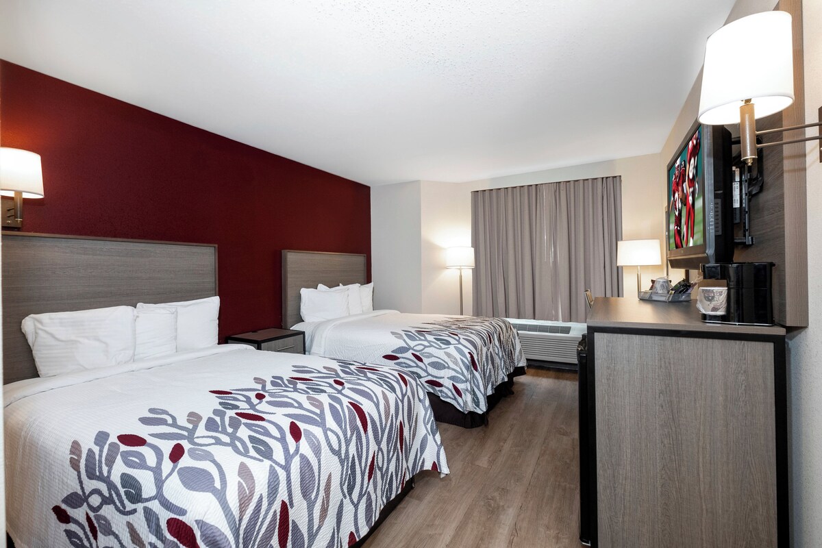 Habitación de hotel con dos camas, un escritorio, un televisor y una ventana con cortinas.