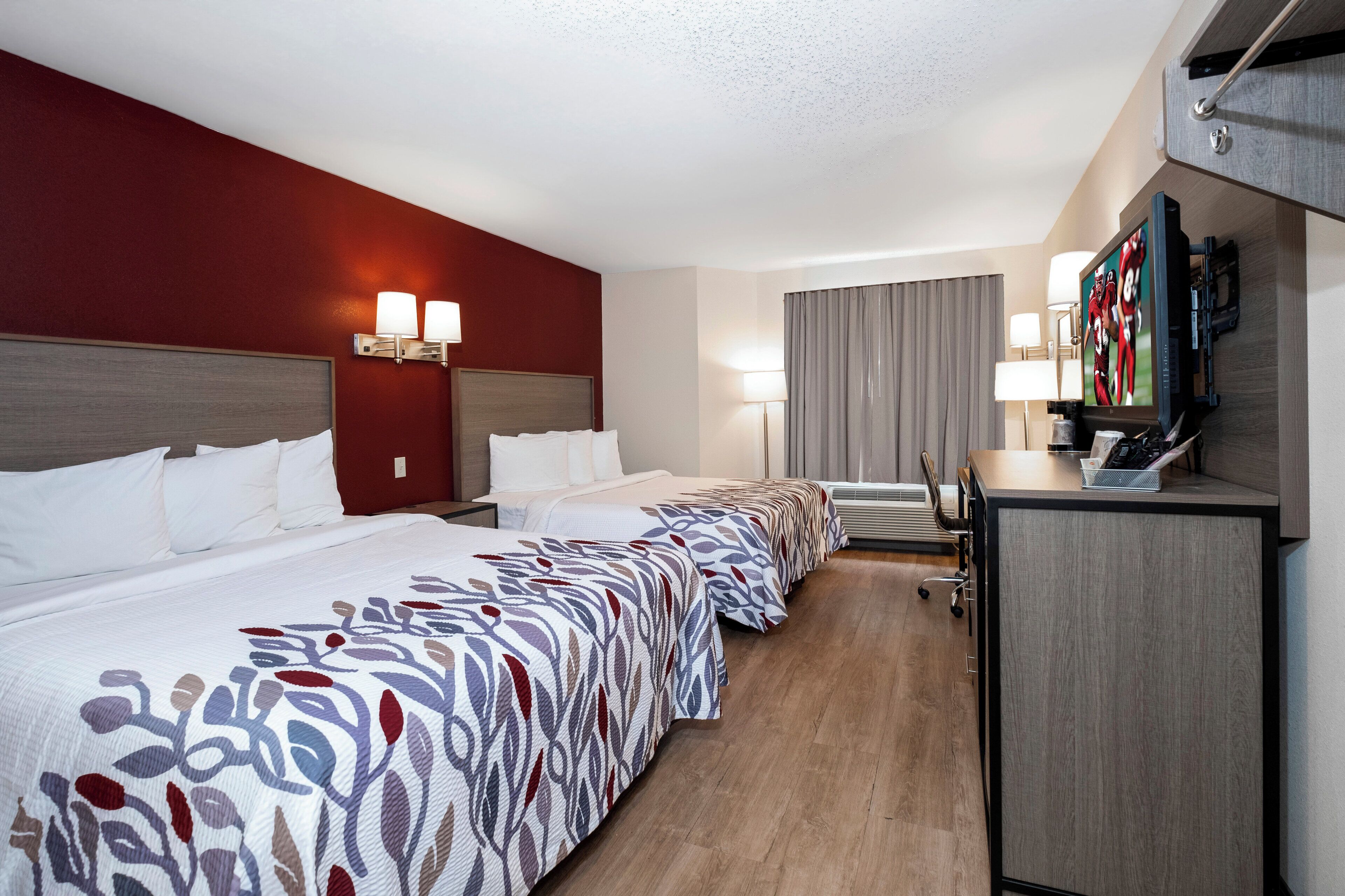 Quarto de hotel com uma cama grande, uma mesa de escritório, televisão e janela com cortinas.