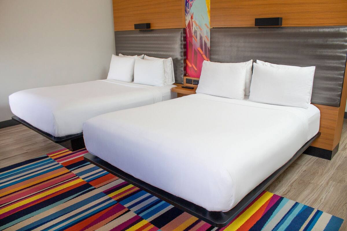 Habitación de hotel con dos camas individuales, un colorido tapiz a rayas y un cabecero moderno.