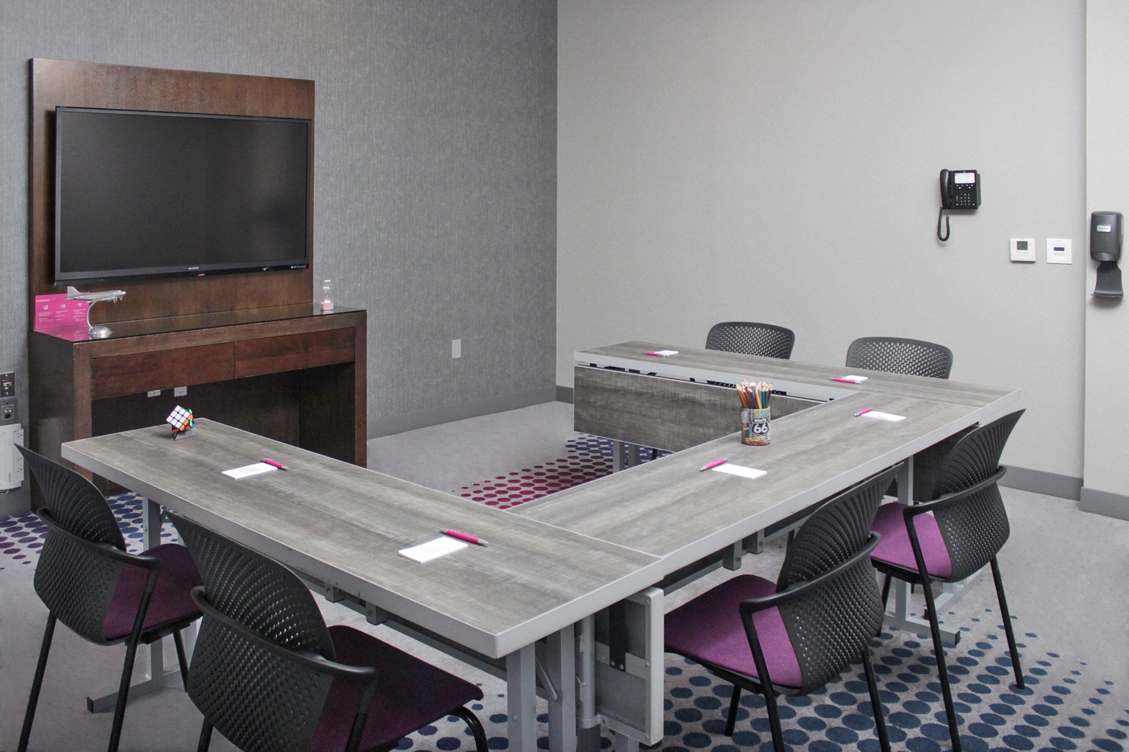 A conference room with a large table, chairs, a TV, and a phone.