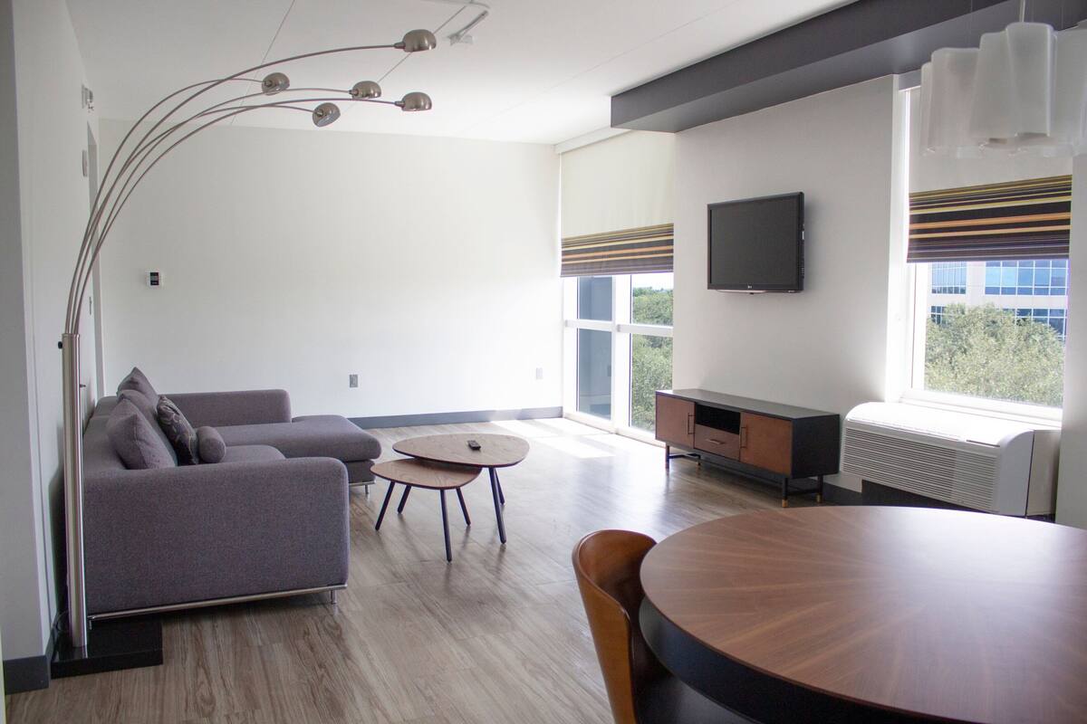 Una sala de estar moderna con un sofá gris, una mesa redonda de madera y un televisor montado en la pared.