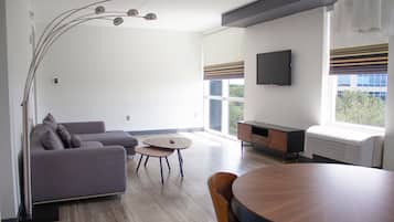 A modern living room with a grey sofa, a round wooden table, and a TV mounted on the wall.