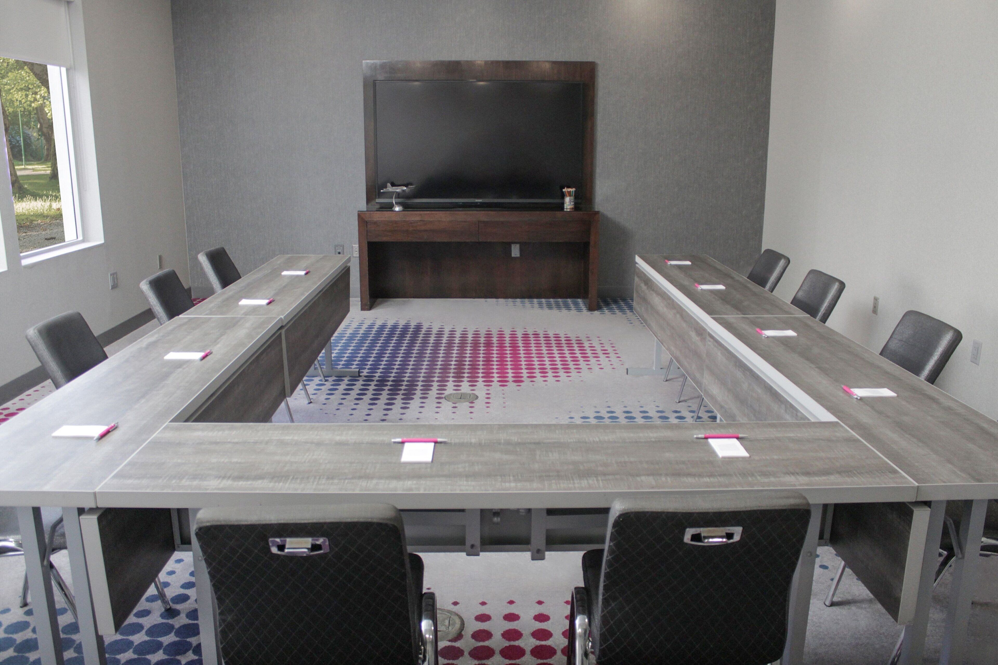 A conference room with a long table, chairs, a TV, and a sink.