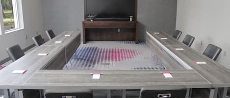A conference room with a long table, chairs, a TV, and a sink.