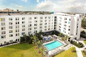 Un hotel moderno con una piscina amplia, mobiliario exterior y un césped cuidado.