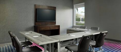 A conference room with a long table, six chairs, a flat-screen TV, and a window with a view of buildings and trees.