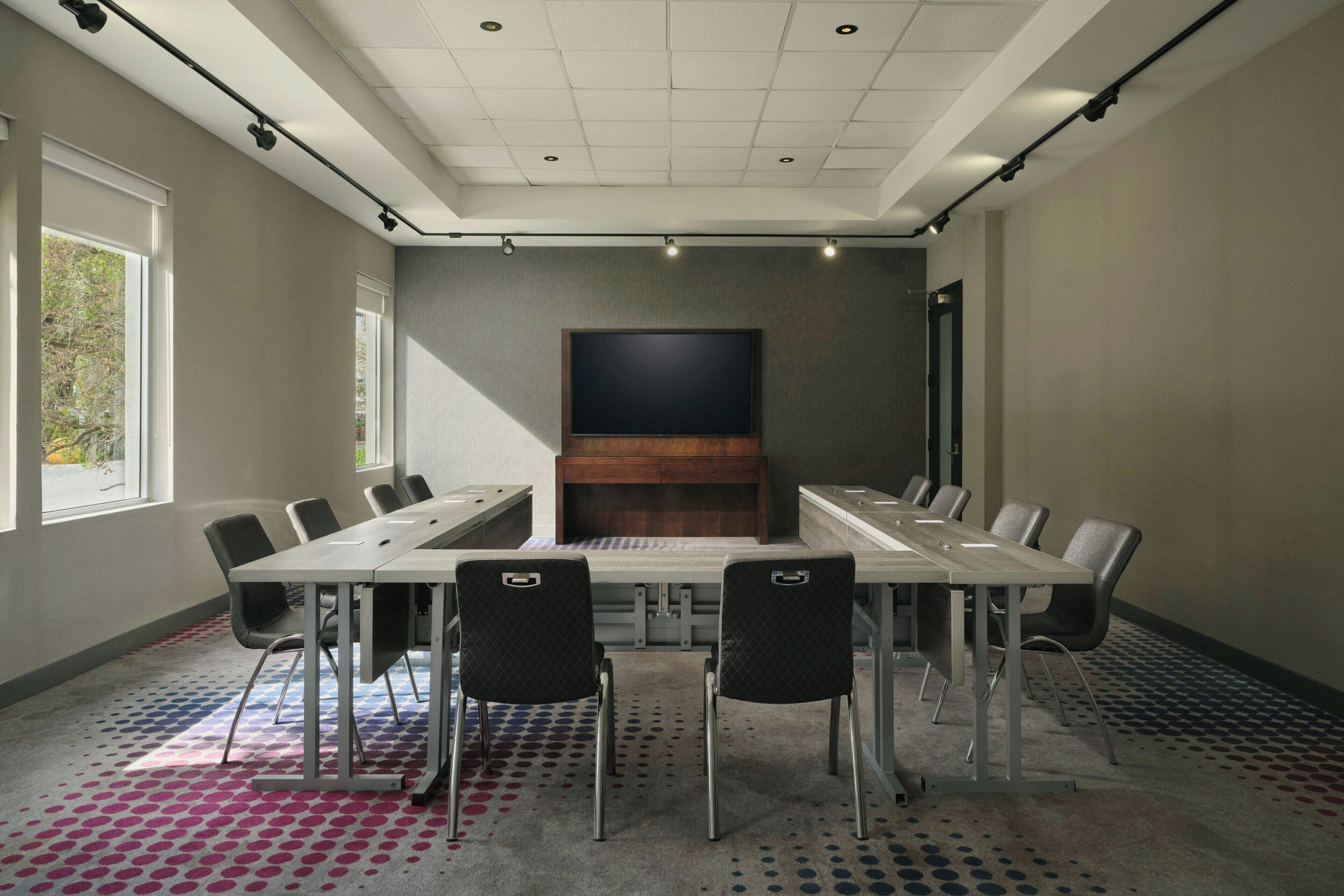 A conference room with a long table, chairs, a large screen, and a patterned carpet.