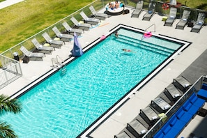 En rektangulär pool med klart, blått vatten, omgiven av solstolar och en uteplats.