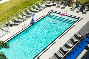 Una piscina rectangular con agua cristalina y azul, rodeada de sillones de descanso y una terraza.