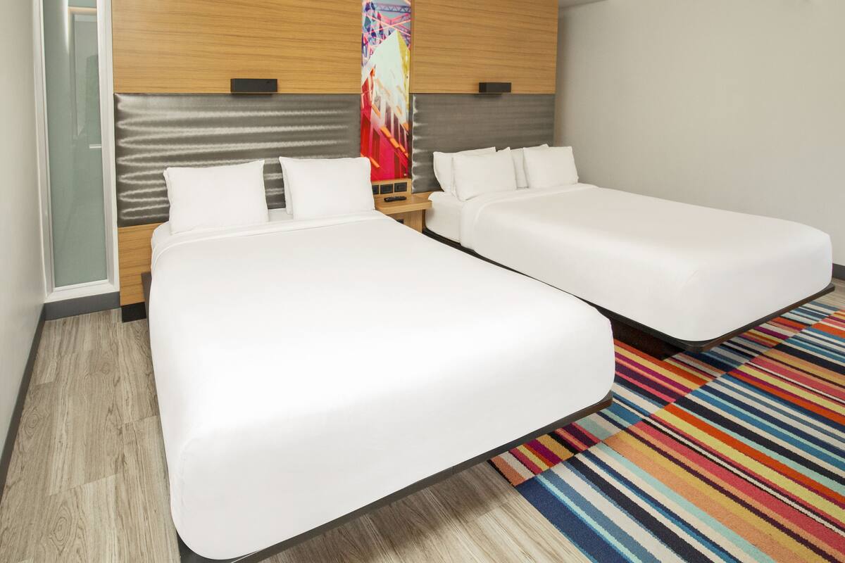 A hotel room with two single beds, a wooden headboard, a colorful striped rug, and a glass partition.