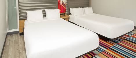 A hotel room with two single beds, a wooden headboard, a colorful striped rug, and a glass partition.