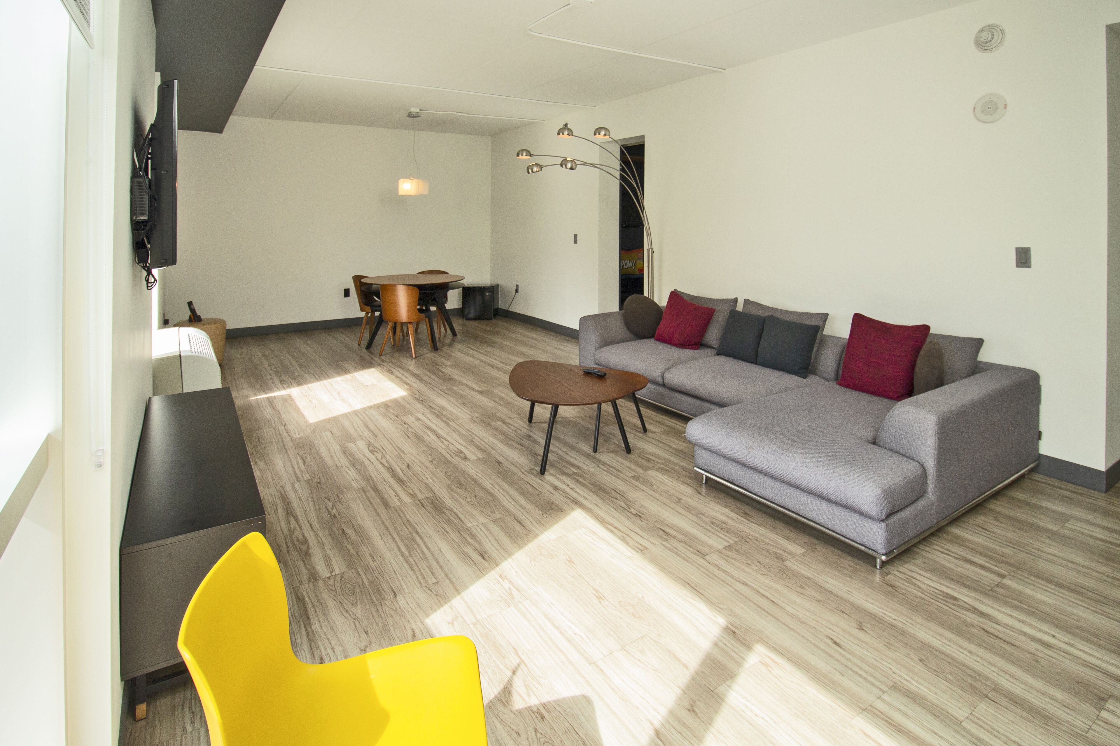 A modern living room with a grey sofa, yellow chair, and a dining area with a table and chairs.