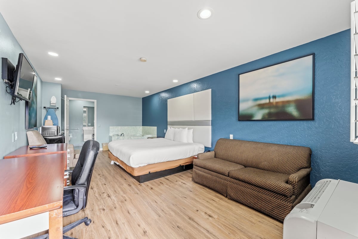 Ett modernt hotellrum med ett skrivbord i trä, en stor säng, en brun soffa och en tv som är monterad på väggen.