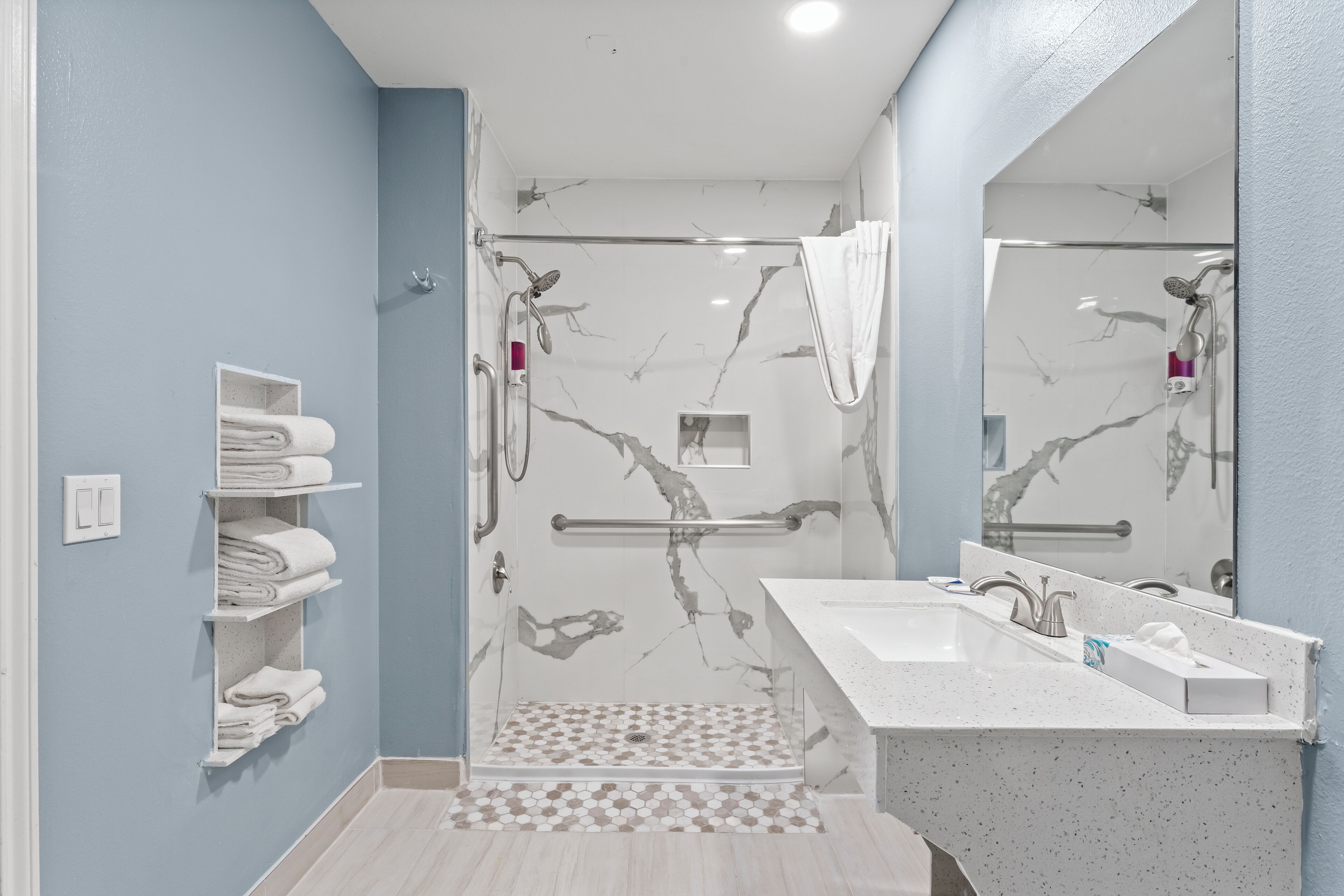 A modern bathroom with a glass-enclosed shower, a white sink with a marble countertop, and a towel rack with neatly folded towels.