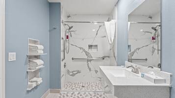 Ein modernes Badezimmer mit einer gläsernen Duschkabine, einem weißen Waschbecken mit Marmorplatte und einem Handtuchhalter mit ordentlich gefalteten Handtüchern.