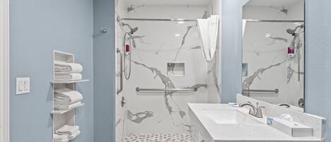 A modern bathroom with a glass-enclosed shower, a white sink with a marble countertop, and a towel rack with neatly folded towels.