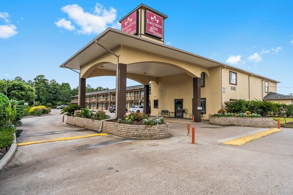 A hotel with a covered entrance, a brick planter with flowers, and a clear blue sky.