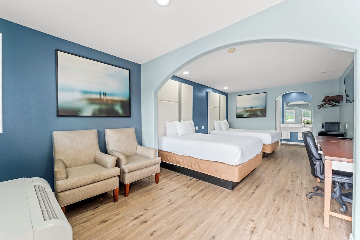 Ett hotellrum med en säng, två stolar, ett skrivbord och en tv.