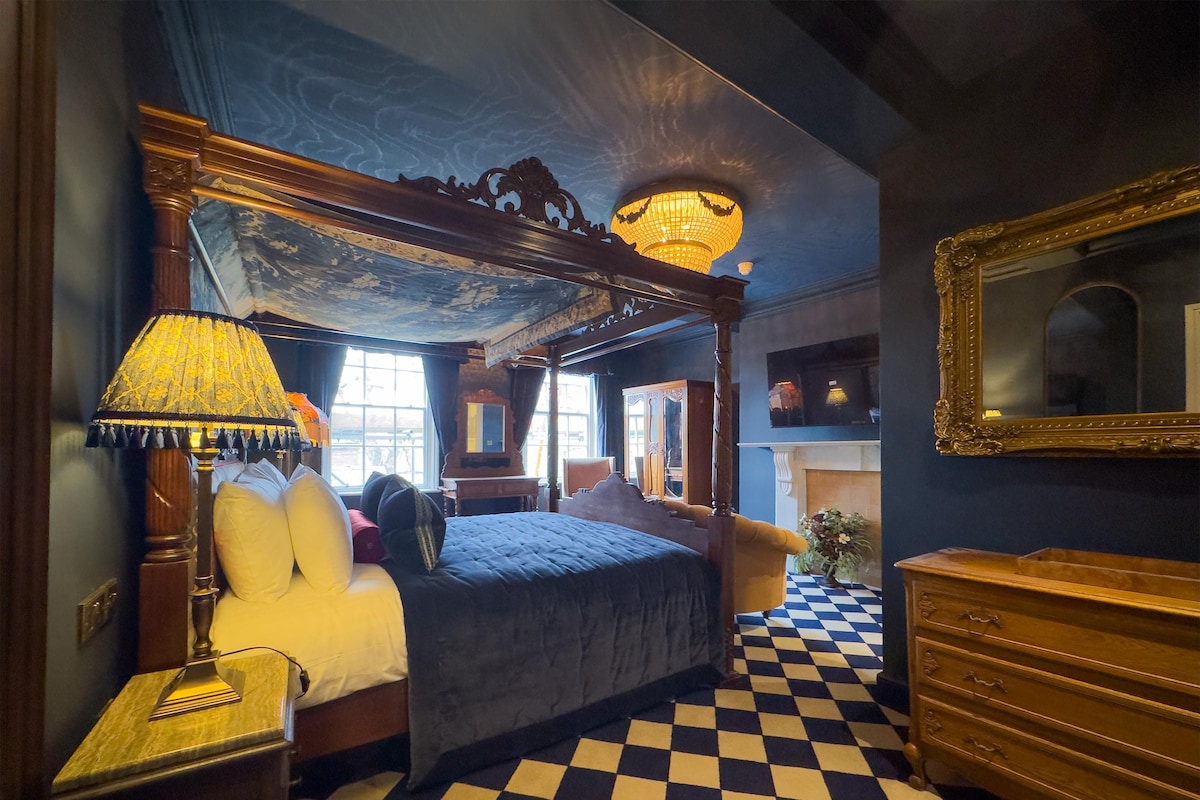 A room with a checkered floor, a four-poster bed, a chandelier, and a large mirror.