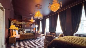 Een kamer met een zwart-wit geruit vloerkleed, een hemelbed, een grote kroonluchter en een televisie.
