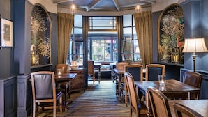 Een eetruimte met houten tafels en stoelen, grote ramen en decoratieve muurdecoratie.