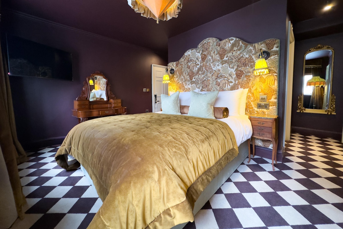 A bedroom with a checkered floor, a large bed with a gold-colored headboard, and a decorative wall panel.